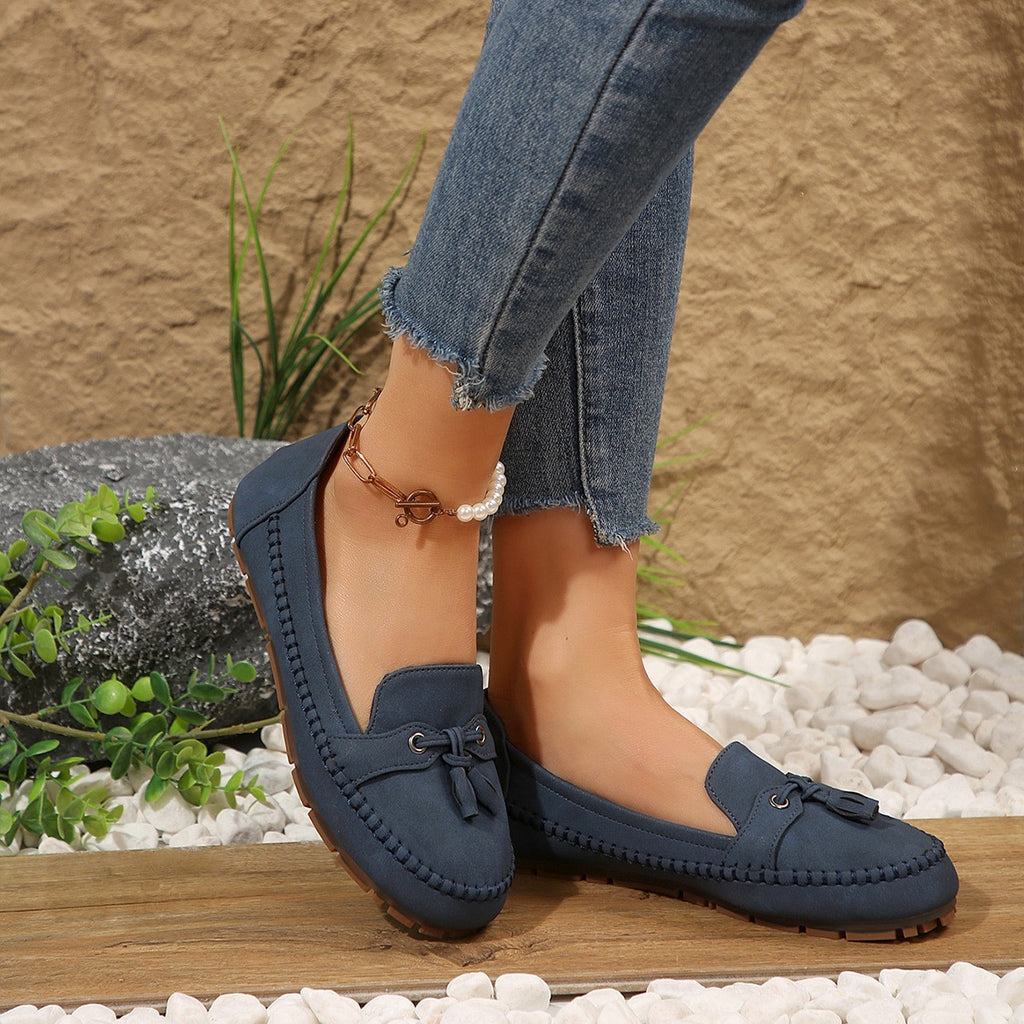 Navy loafers worn with ripped jeans against a natural stone background