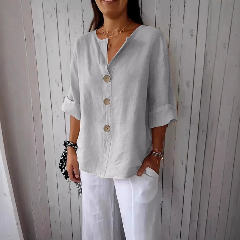 Woman wearing a light blue button-up shirt and white pants against a wooden wall.