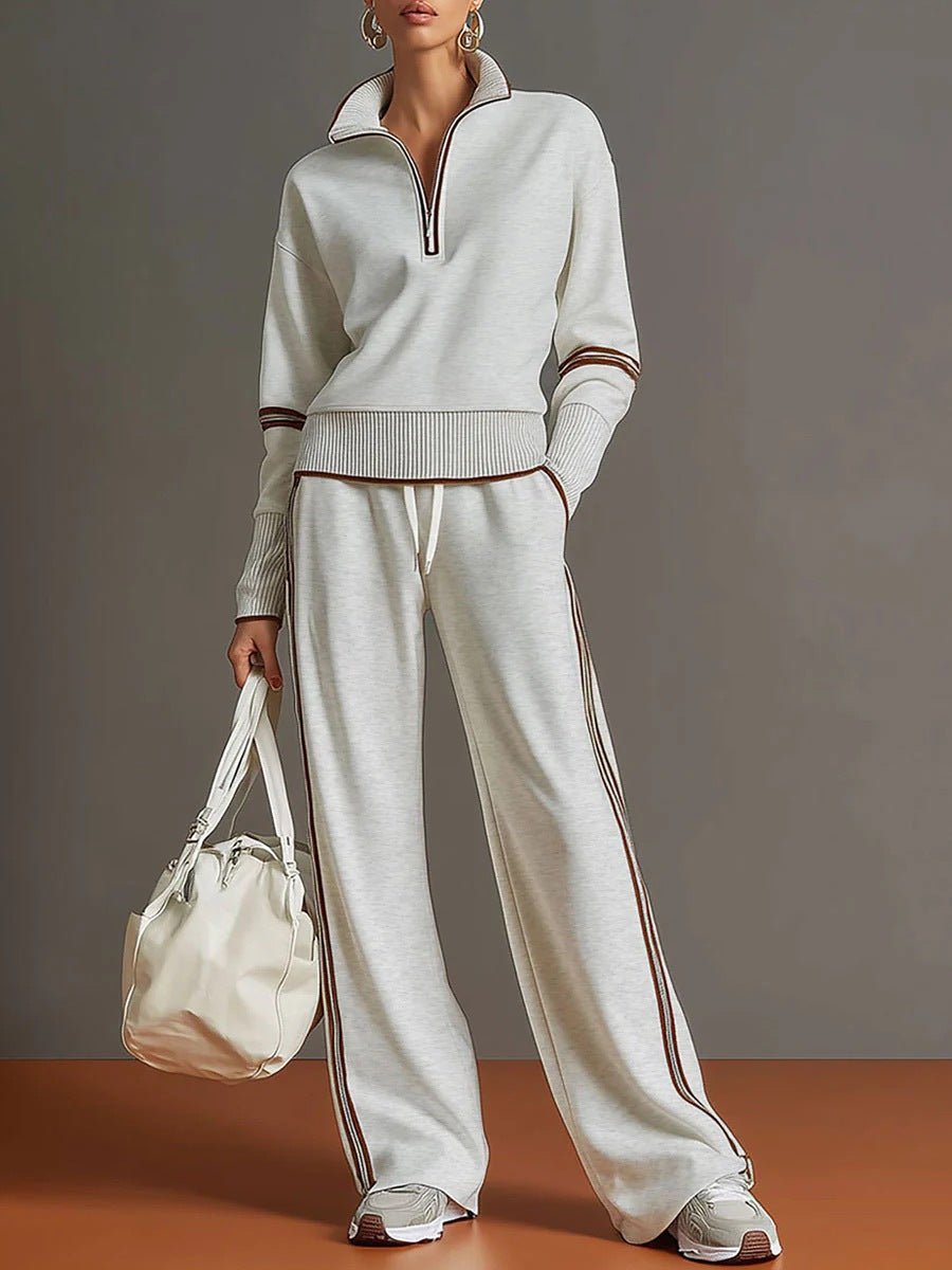 Person wearing a light gray tracksuit with brown accents, holding a matching bag against a gray background.