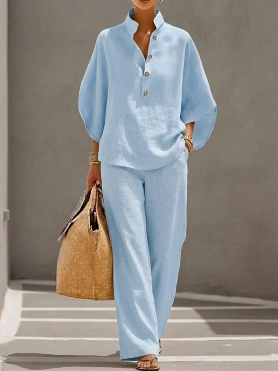 Person wearing a light blue outfit with wide-leg pants, holding a straw bag against a neutral background.