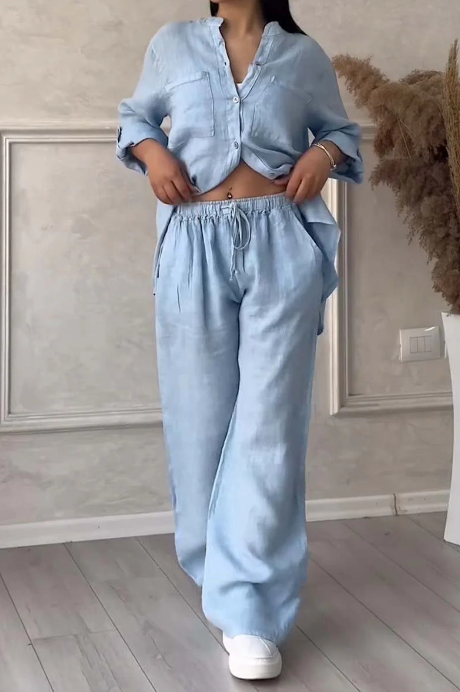 Person wearing a light blue outfit with a shirt and pants in a minimalistic room.