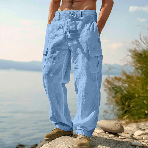 Person wearing light blue cargo pants standing by a body of water with mountains in the background.