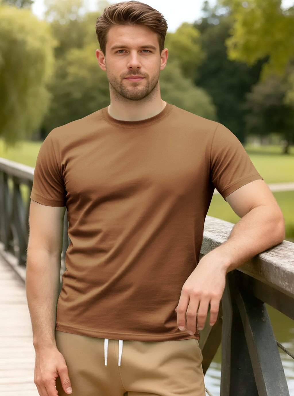 Man wearing a brown t-shirt and beige pants standing outdoors with greenery in the background