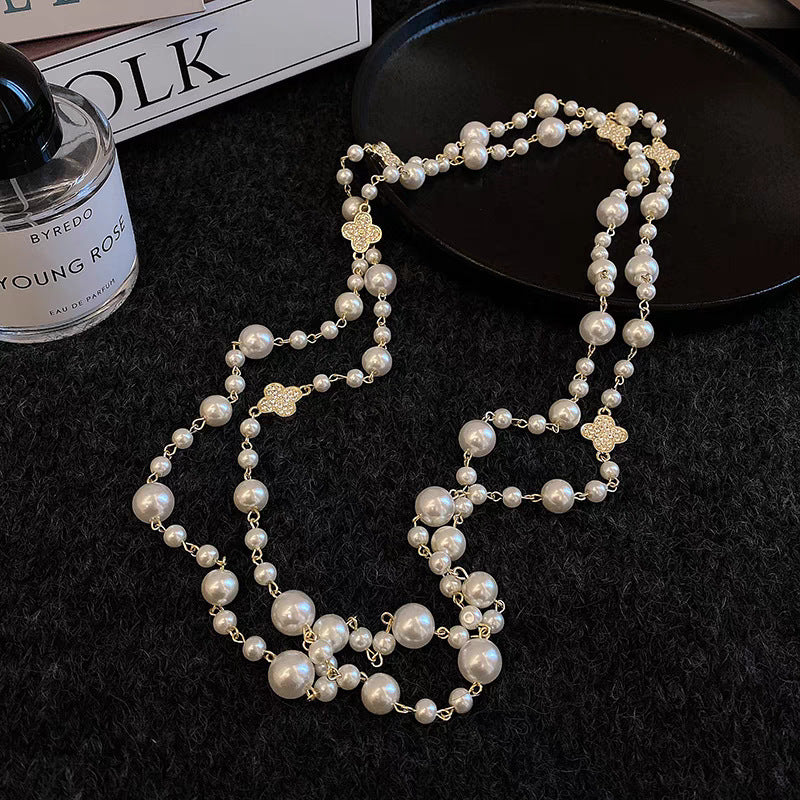 Pearl necklace on a dark surface with a Byredo perfume bottle in the background
