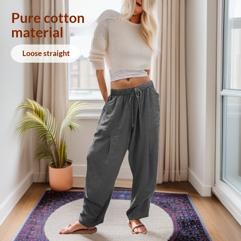 Woman wearing gray loose straight pants in a room with a plant and window.