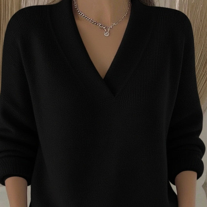 Person wearing a black sweater with a deep neckline and a necklace.