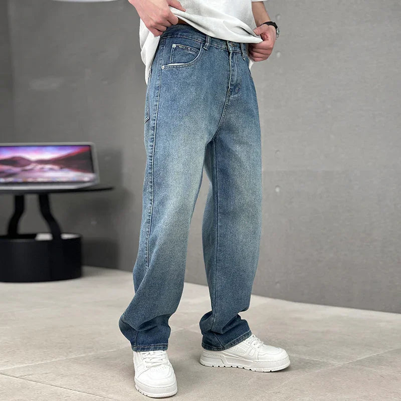 Person wearing blue jeans and white sneakers in a minimalistic setting with a laptop in the background.