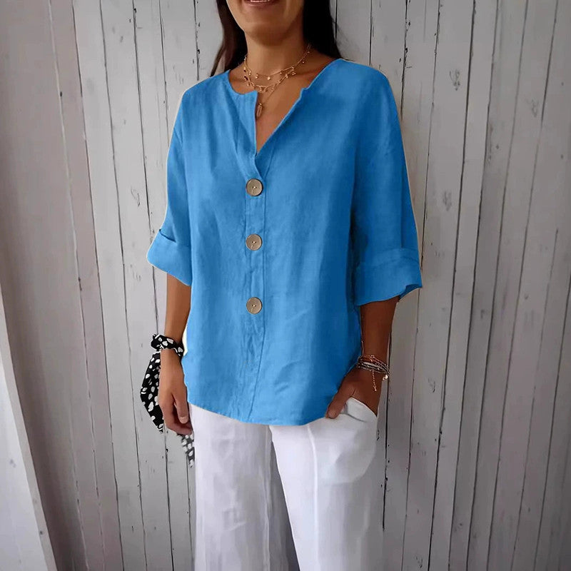 Woman wearing a blue button-up shirt and white pants against a wooden wall.