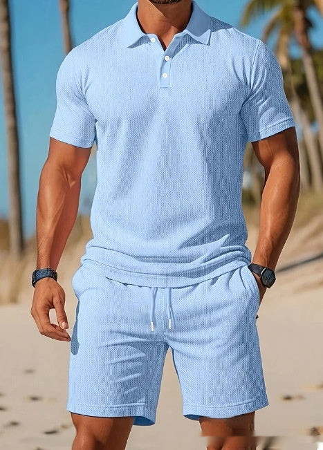 Man wearing a light blue textured polo shirt and shorts on a beach.