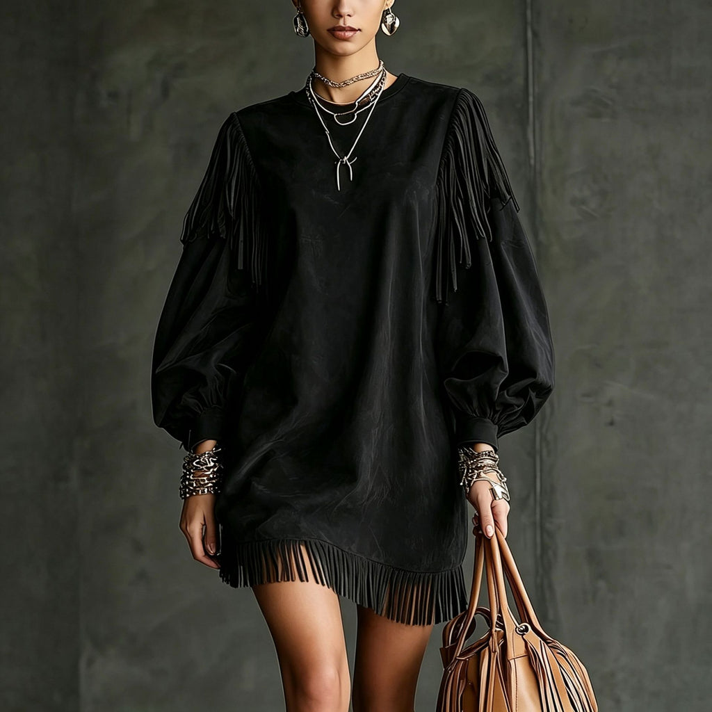 A model wearing a black fringe mini dress with voluminous balloon sleeves, accessorized with layered silver necklaces, bracelets, and earrings, holding a brown leather tote bag against a dark gray textured wall.