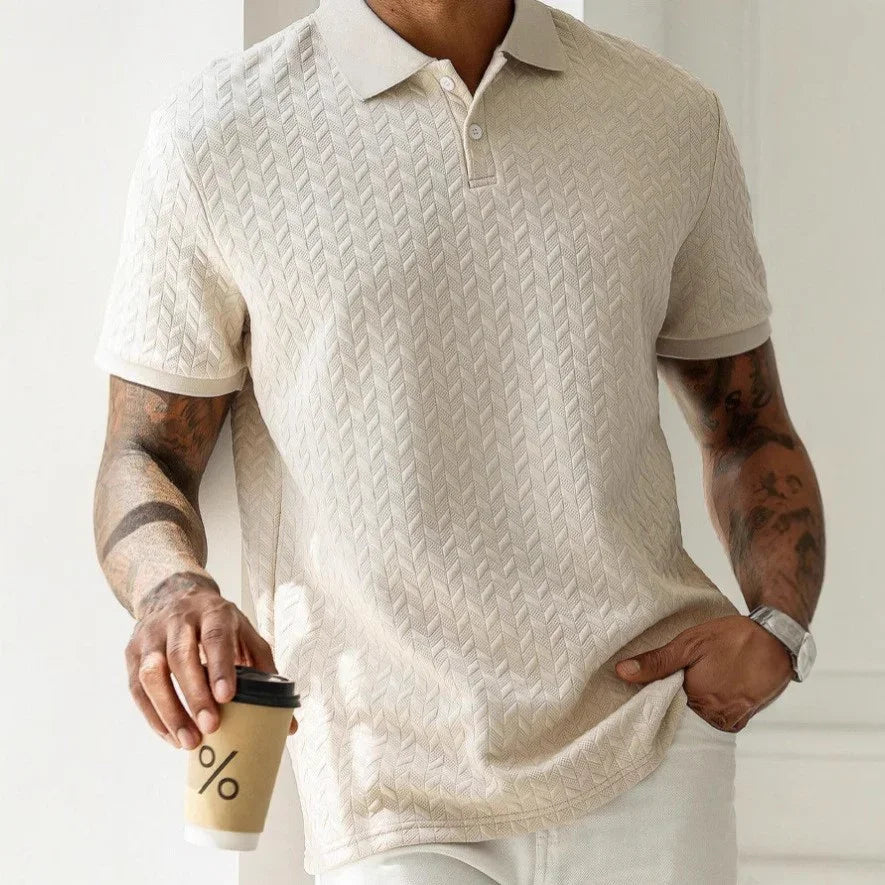 Man wearing a beige patterned polo shirt holding a coffee cup.
