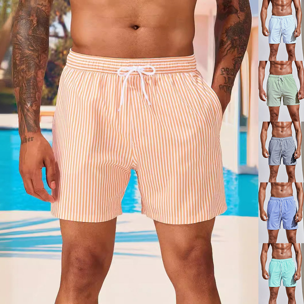 Man wearing striped swim shorts with a pool in the background, surrounded by other men in different swim shorts.