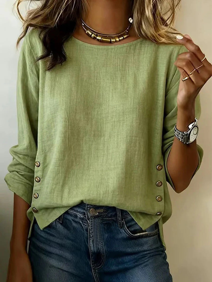Person wearing a green long-sleeve top with button details and blue jeans on a plain background