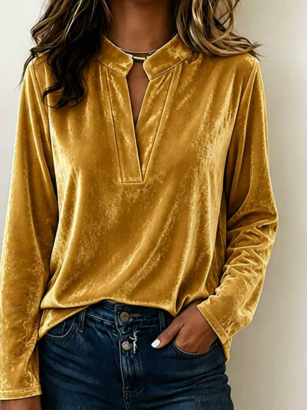A woman wearing a mustard yellow velvet long-sleeve blouse with a split V-neckline, paired with dark blue jeans.