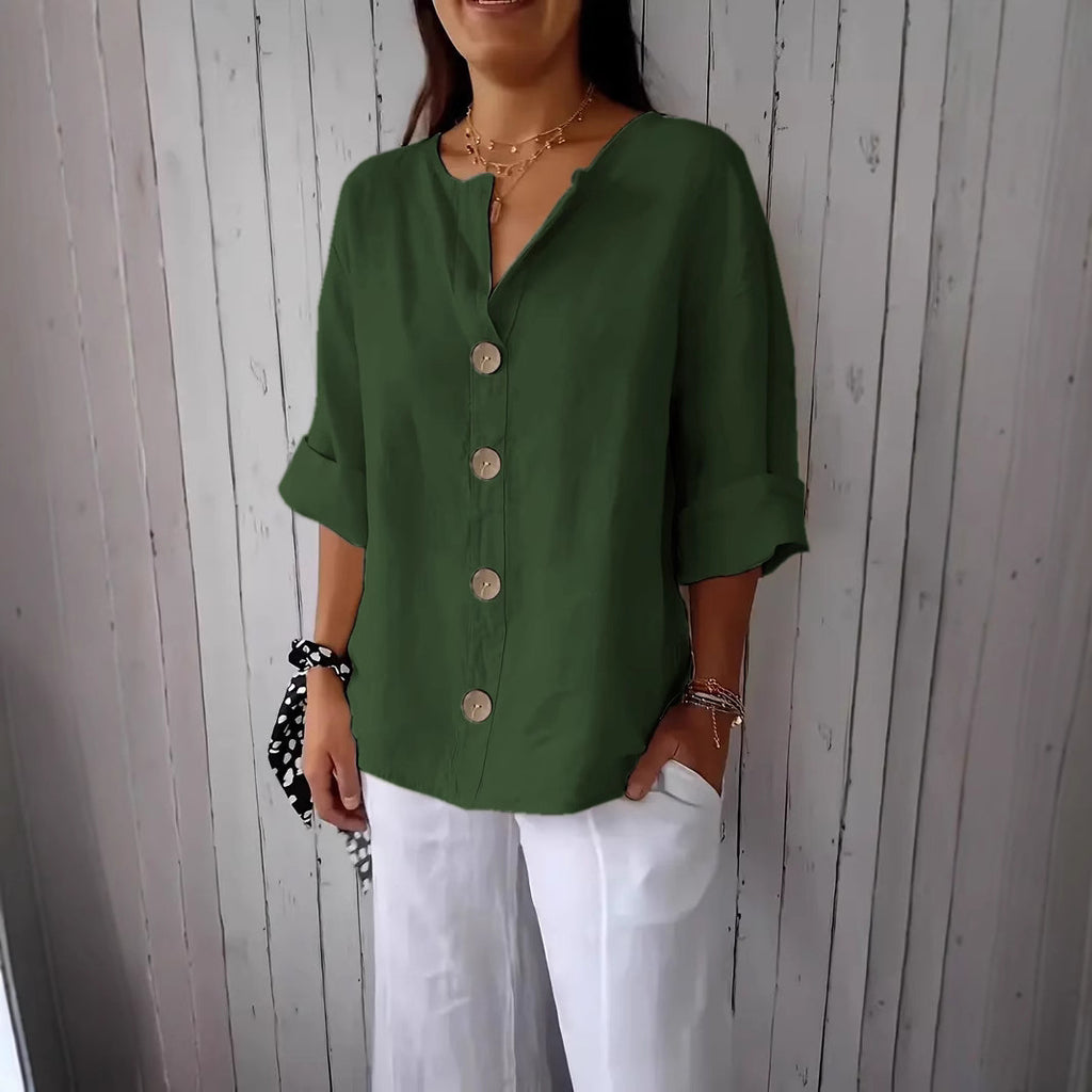 Woman wearing a green button-up shirt and white pants against a wooden panel background