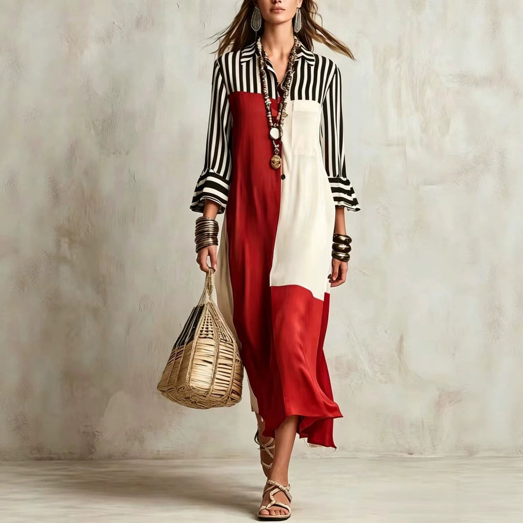 A woman models a long-sleeve color-blocked dress with a black and white striped shirt-style top, a red lower panel, and an off-white central panel. She is accessorized with layered necklaces, bracelets, and a woven straw handbag, standing against a textured light gray wall.