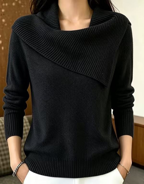 A woman wearing a black long-sleeve knit sweater with an asymmetrical draped cowl neckline, paired with white pants.