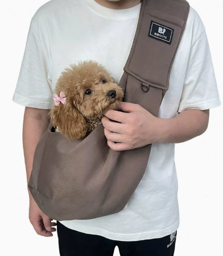 Person holding a small brown dog in a brown pet sling against a white background