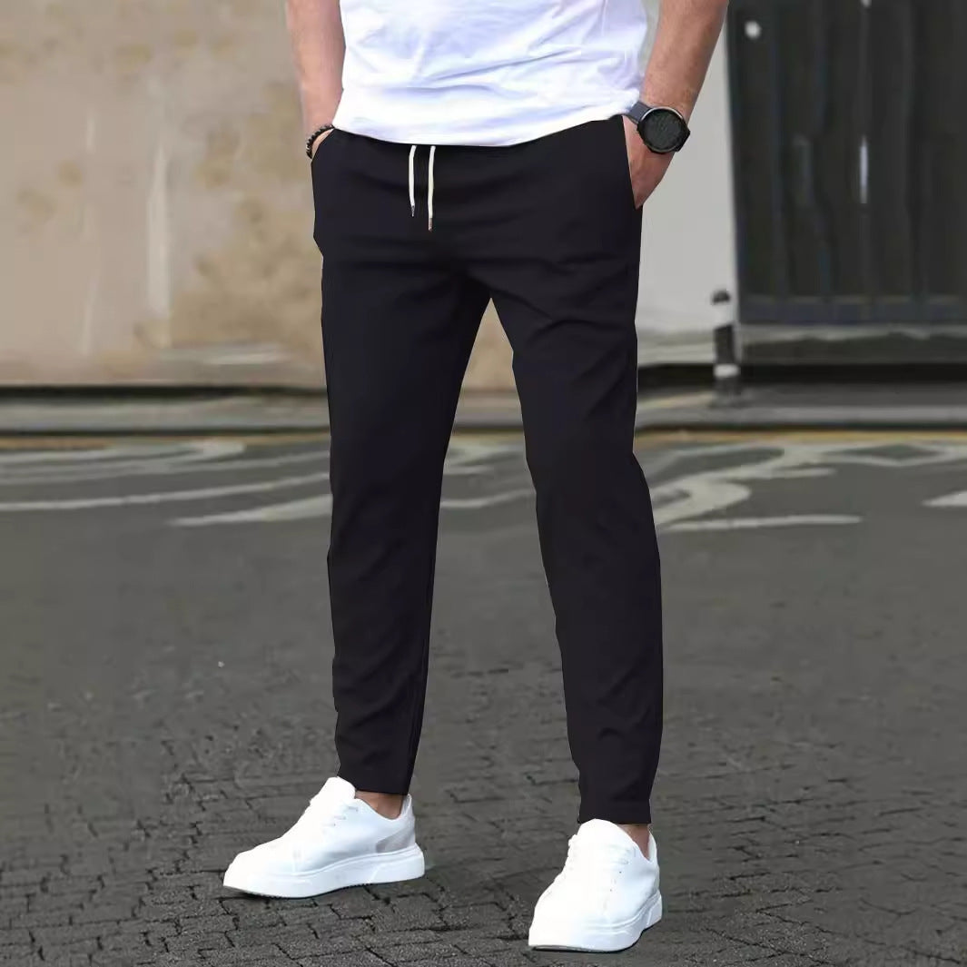 Person wearing black pants and white sneakers on a street.