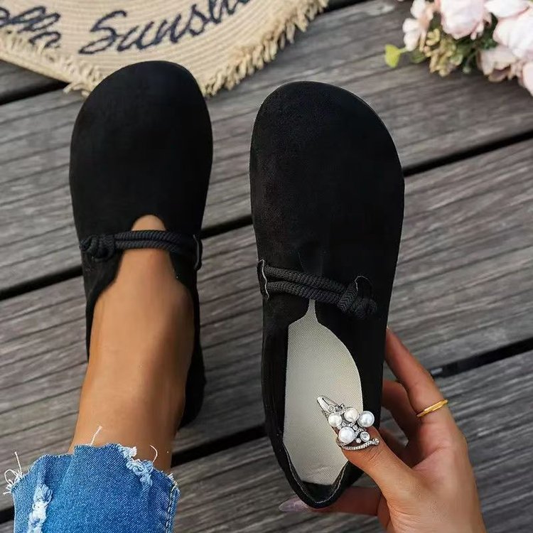 Black loafers worn with rolled-up jeans on a wooden surface.