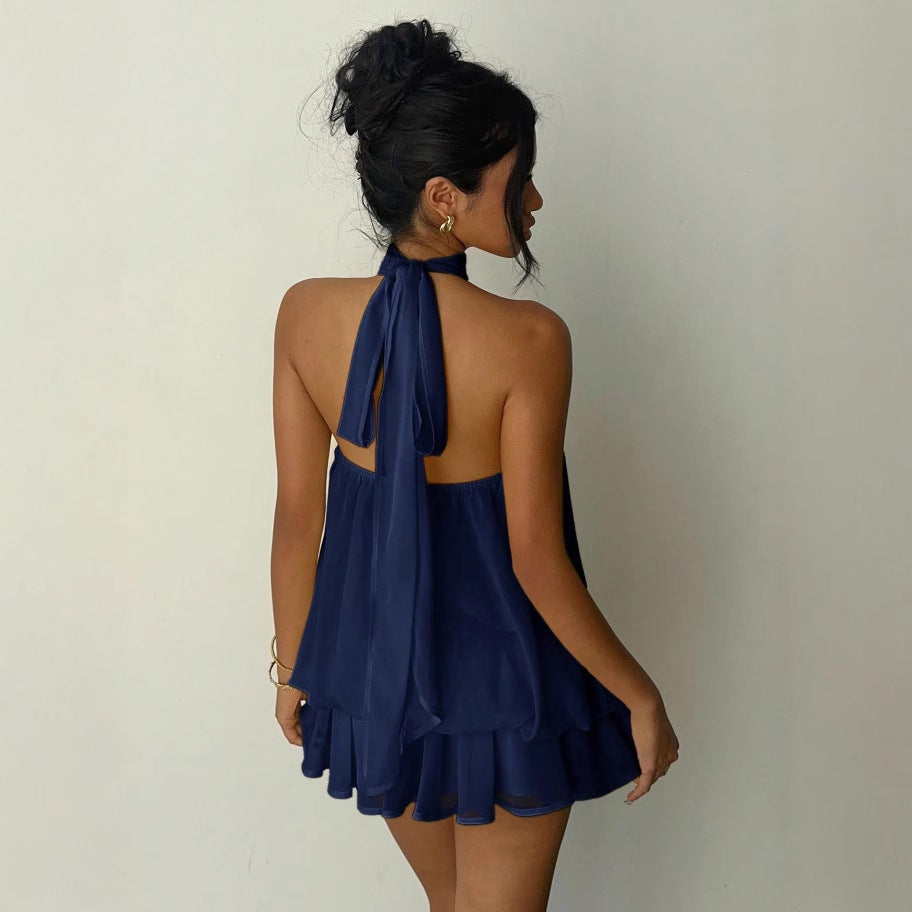 Woman wearing a navy blue halter dress with a tied back detail on a plain background