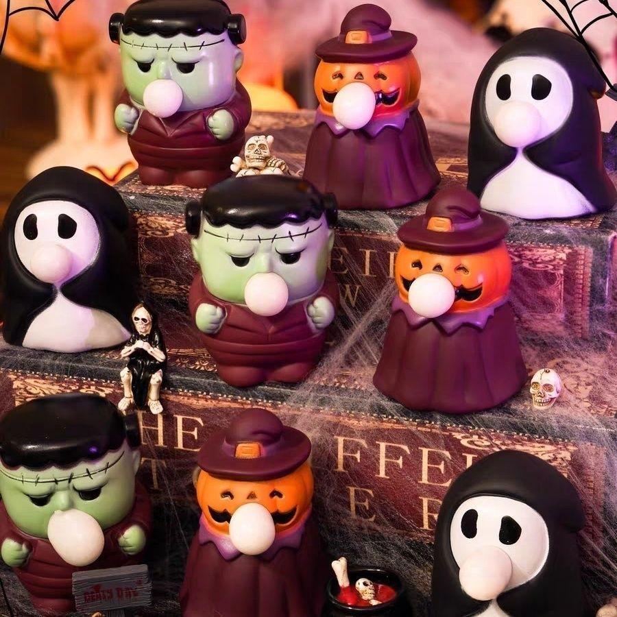 A group of Halloween-themed collectible figurines arranged on a book with cobwebs, including a green Frankenstein character, orange jack-o'-lantern characters, and black-and-white ghostly figures.