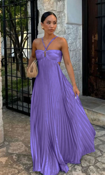 Woman in a purple dress standing outdoors near a stone wall.