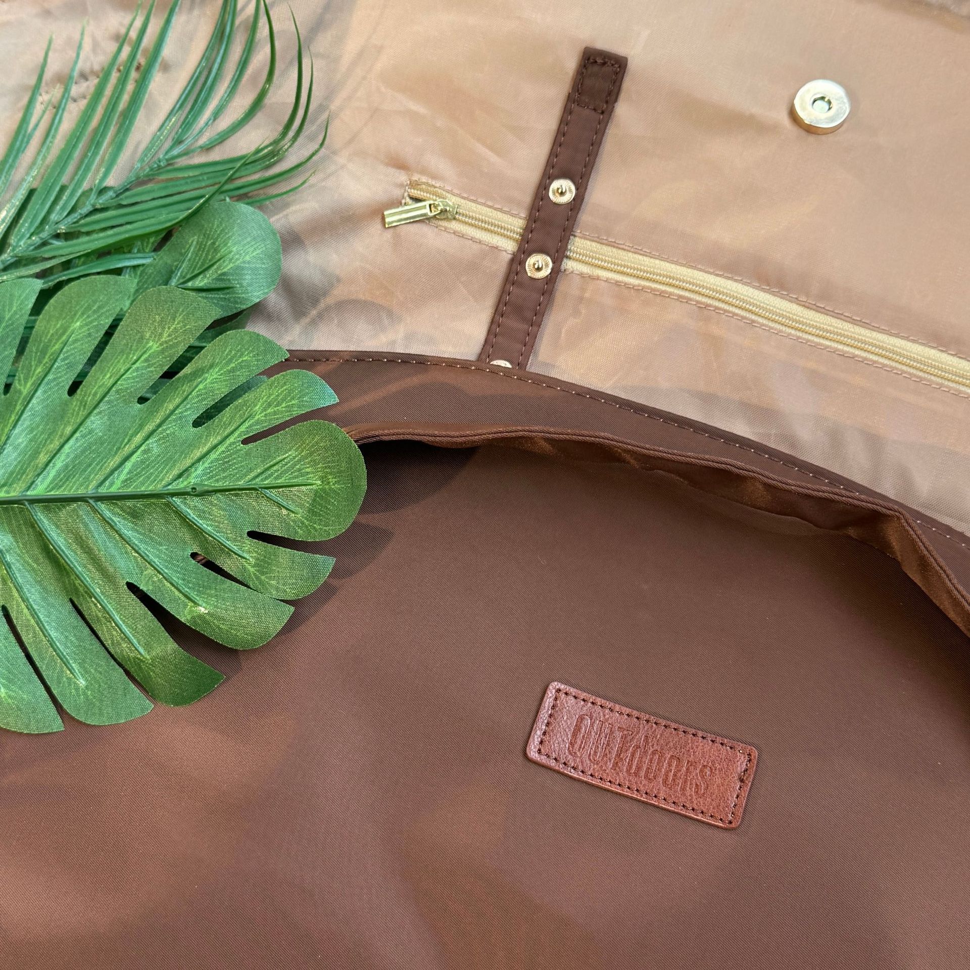 Brown leather bag with a visible brand logo and a green leaf on a matching brown background