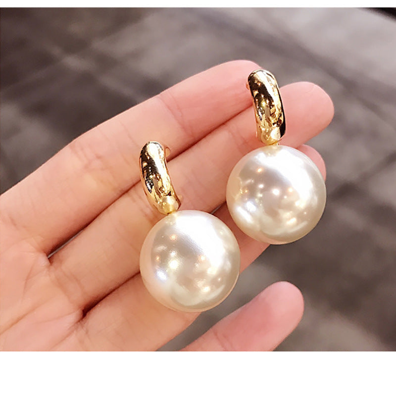 Pearl earrings with gold hooks held in a hand against a blurred background