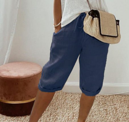 Person wearing blue shorts and a white top, holding a straw handbag indoors.
