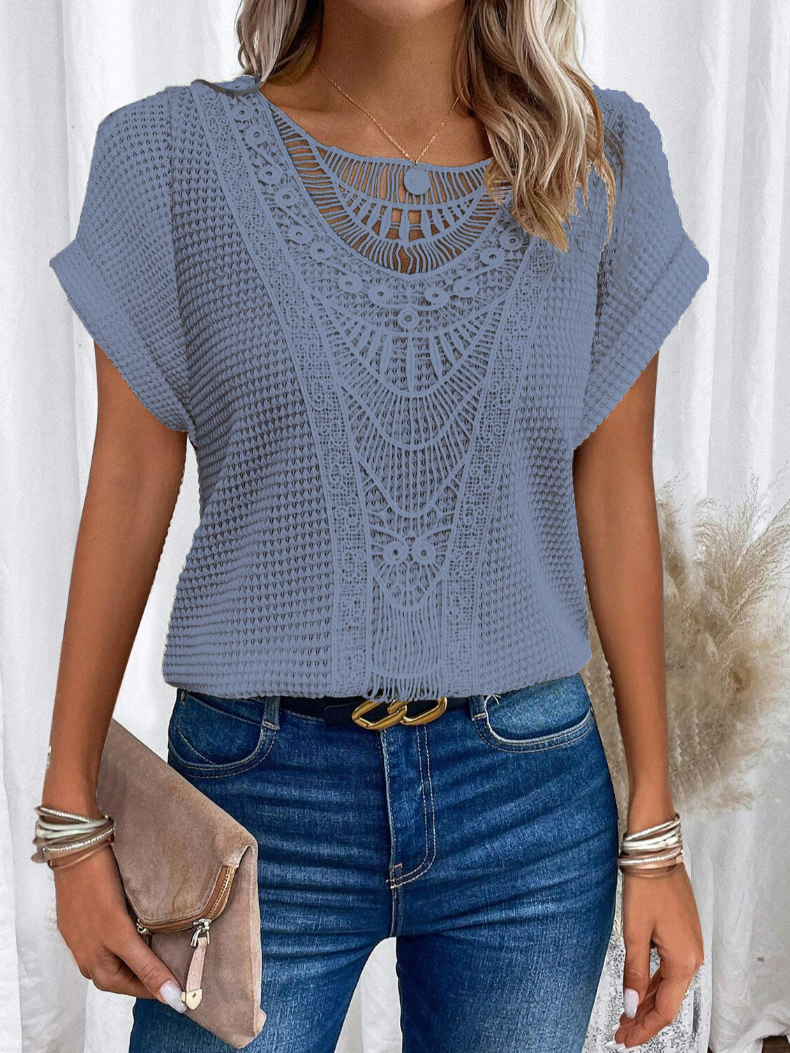 Woman wearing a blue crochet top and jeans with a white curtain background
