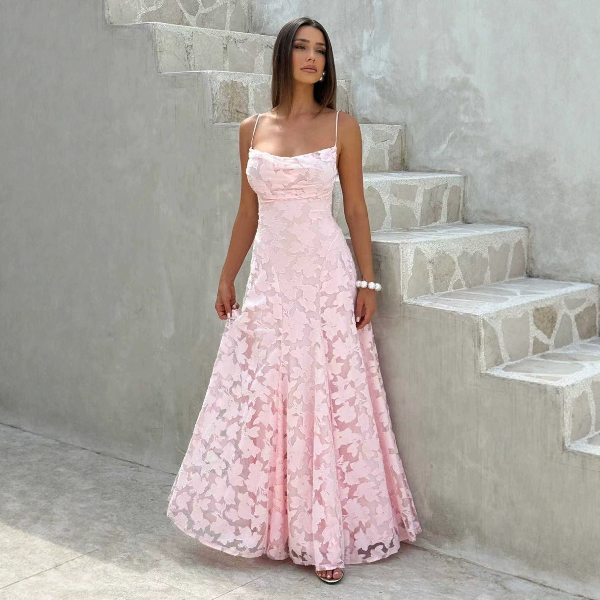 Woman in a pink lace dress standing on stone steps.