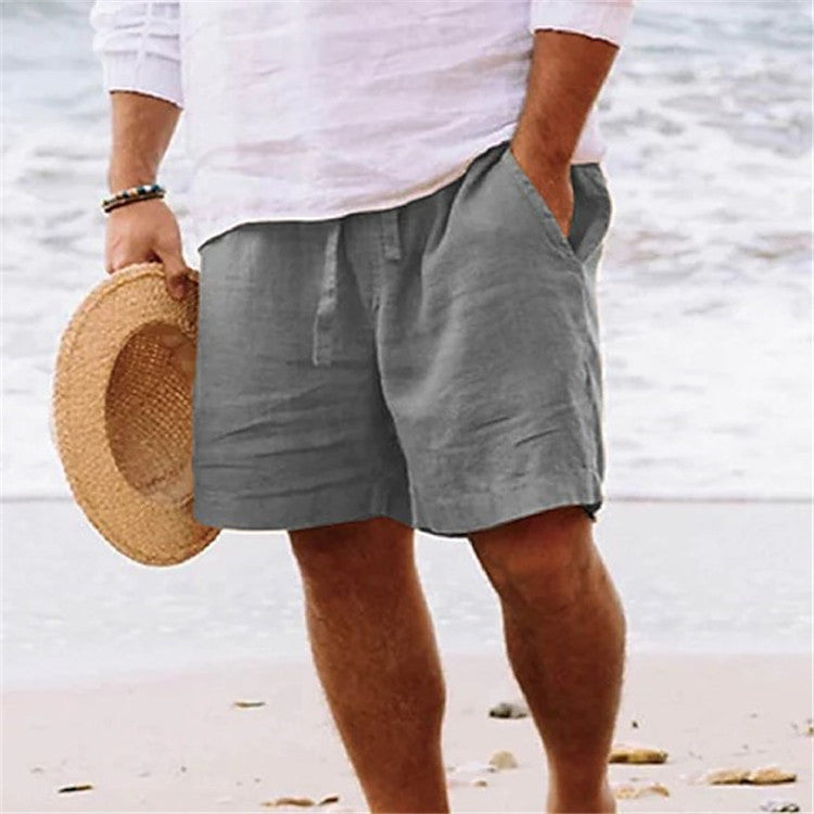 Person wearing gray shorts and holding a straw hat on a beach.