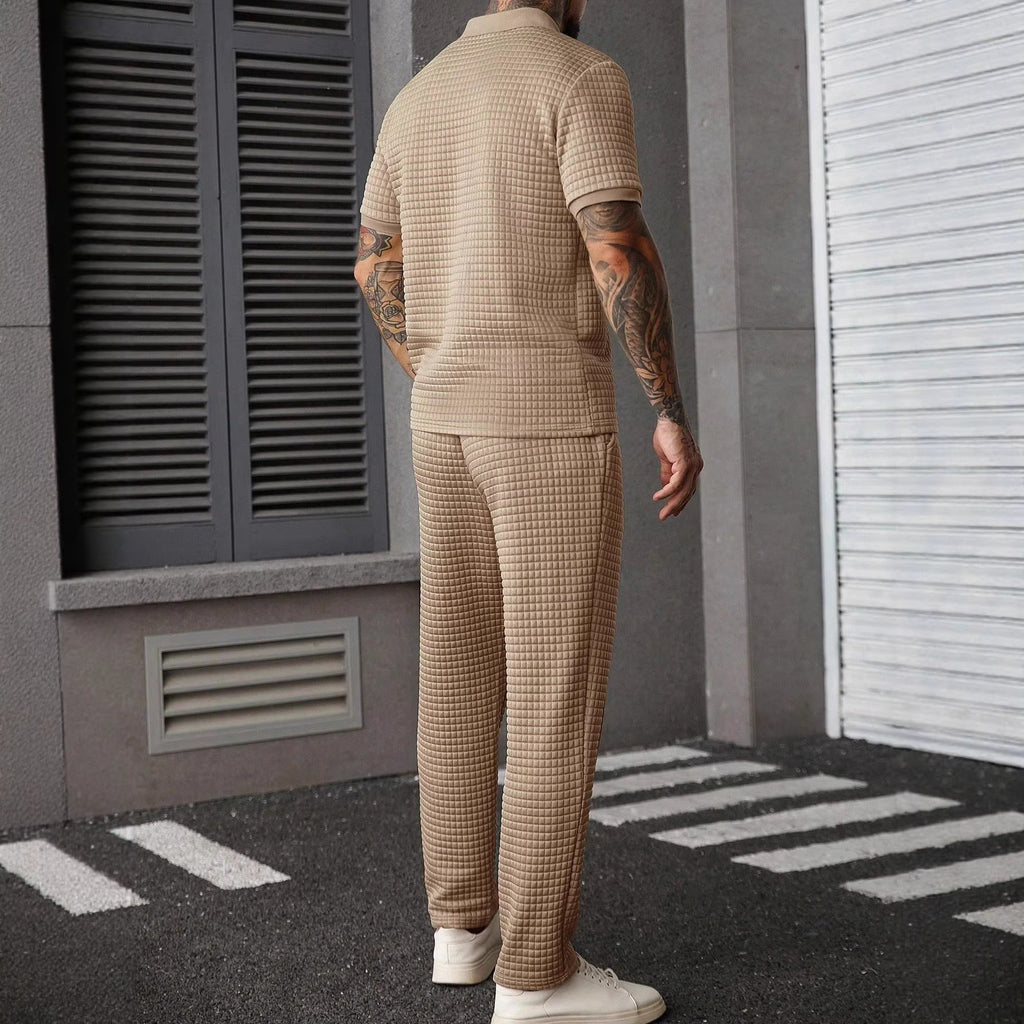 Man wearing a beige checkered outfit standing on a street.