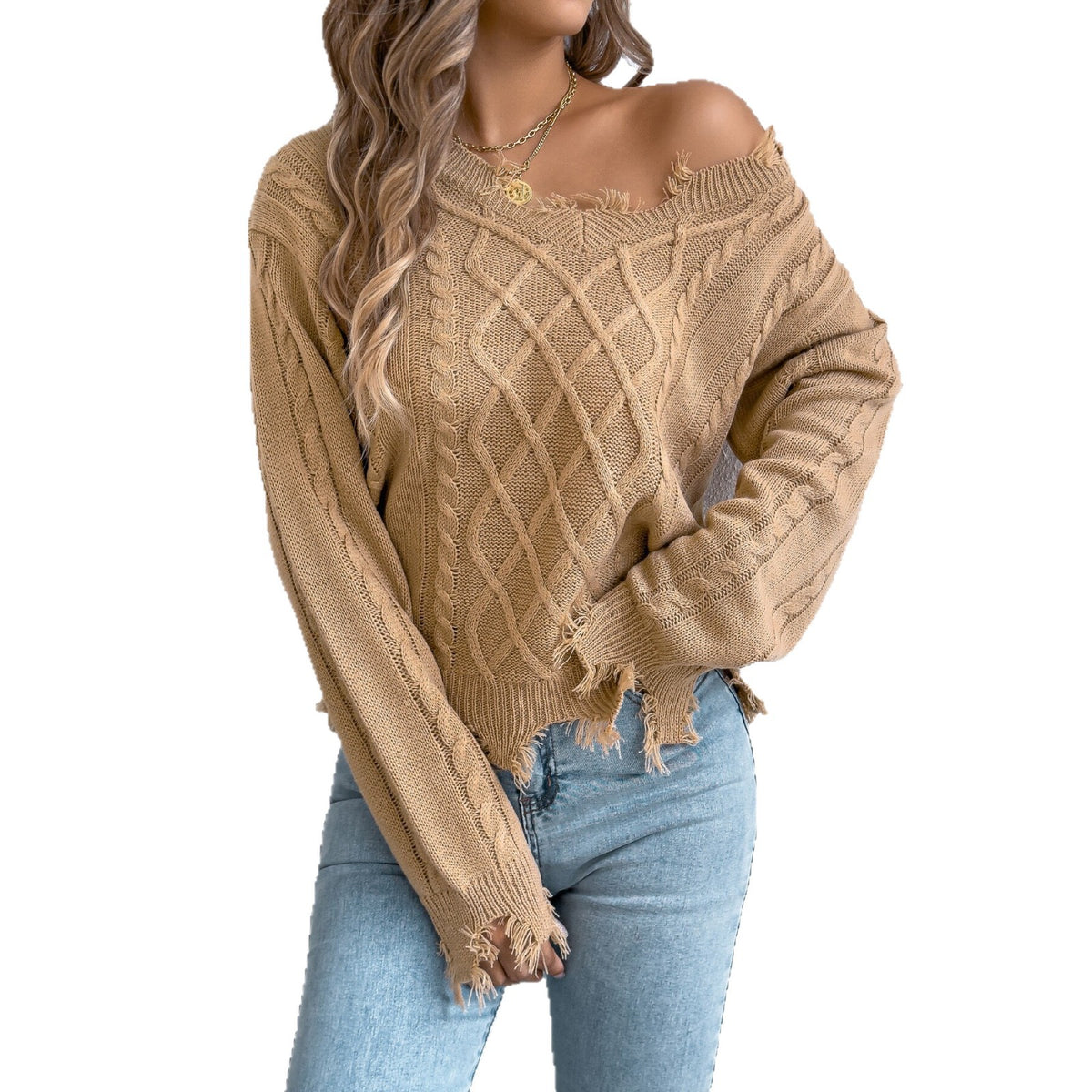A woman wearing a beige off-the-shoulder cable-knit sweater with frayed hems and light blue jeans, shown against a plain white background.