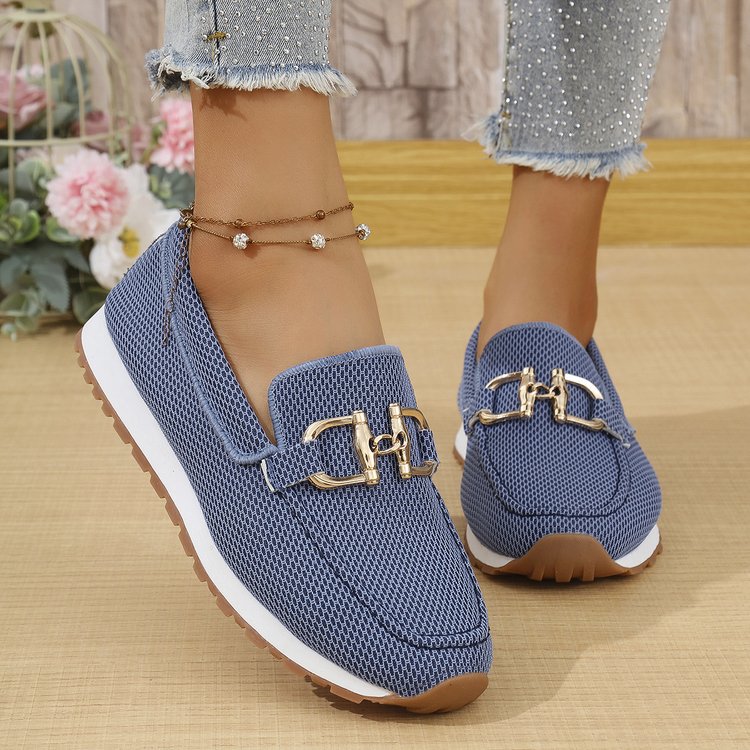 Blue loafers with gold buckles worn by a person on a wooden floor.