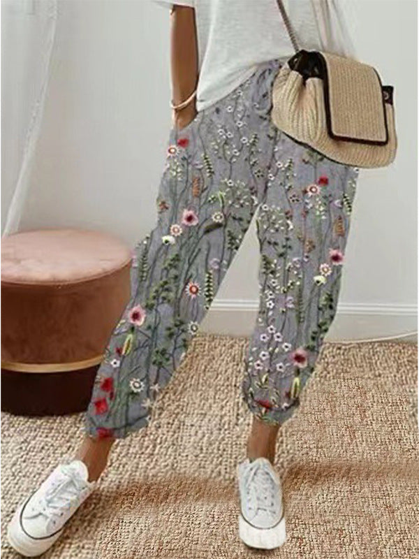 Person wearing floral gray pants with a white top and white sneakers, holding a beige bag.