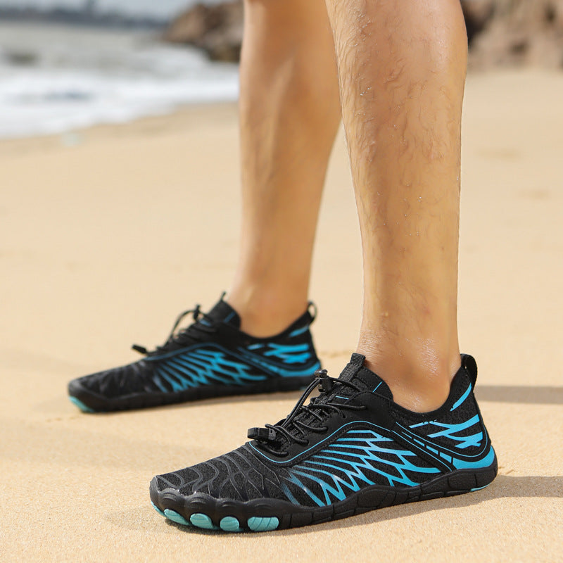 Black and blue water shoes on a person's feet standing on sand with a blurred beach background