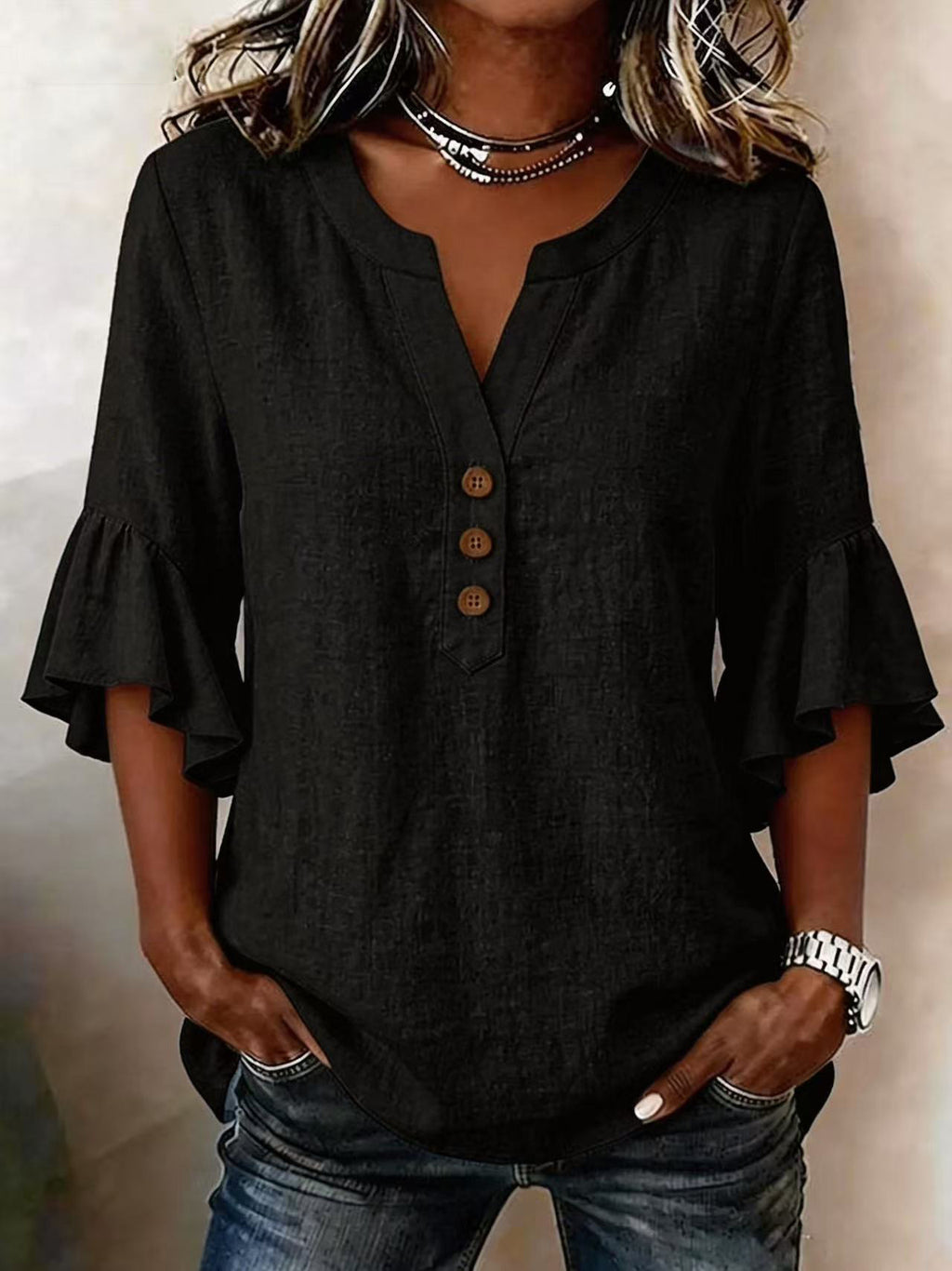 Person wearing a black blouse with ruffled sleeves and jeans against a neutral background