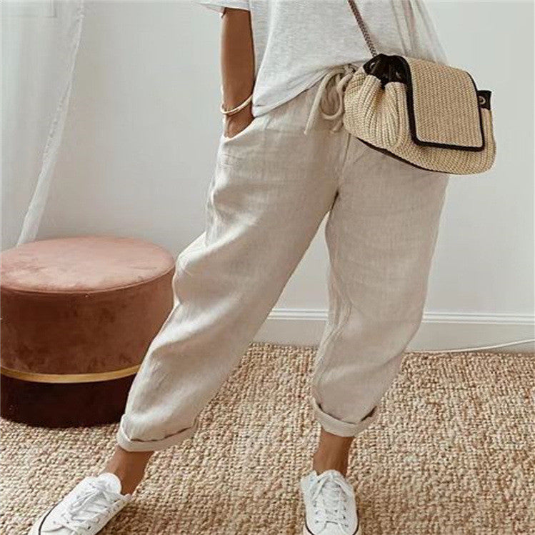 Person wearing beige pants and white sneakers with a straw bag indoors.