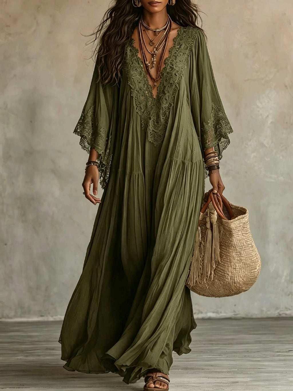 Woman wearing a long green dress with lace details, holding a woven bag against a neutral background.