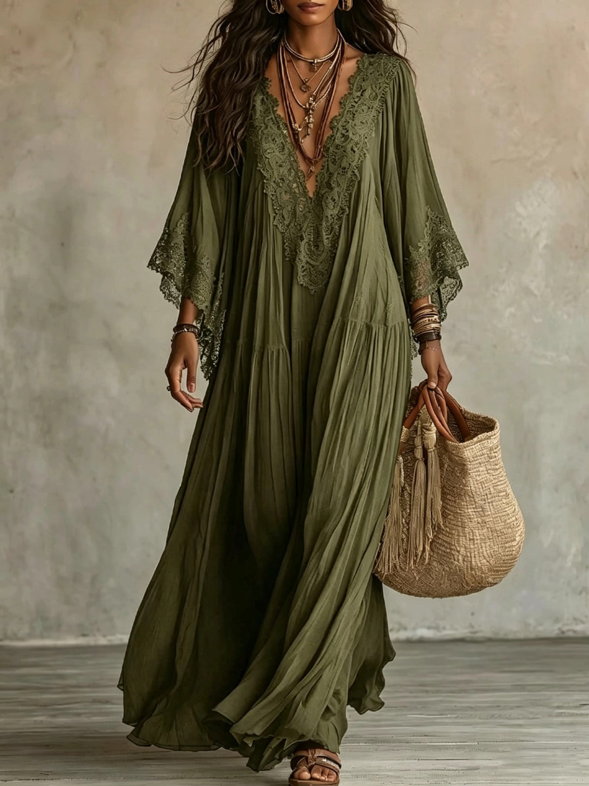 Woman wearing a long green dress with lace details, holding a woven bag against a neutral background.