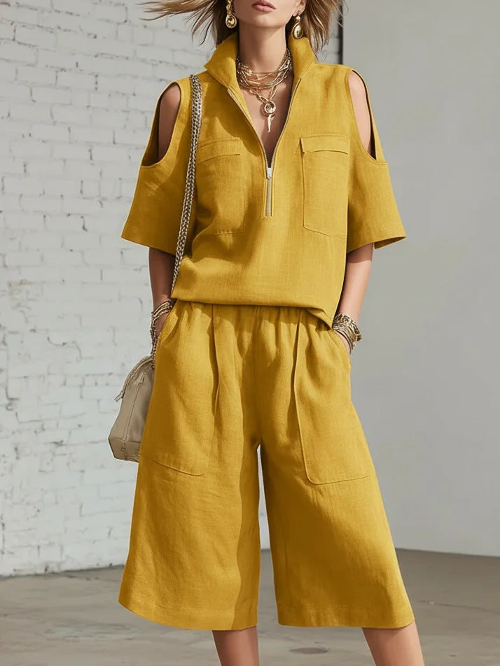 Person wearing a mustard yellow sleeveless top and wide-leg pants against a white brick wall.