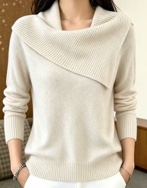 A woman wearing a cream-colored knit sweater with a wide draped cowl neckline, ribbed cuffs, and a ribbed hem, paired with white pants.