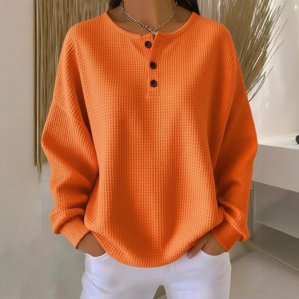 Person wearing an orange textured sweater with black buttons against a neutral background