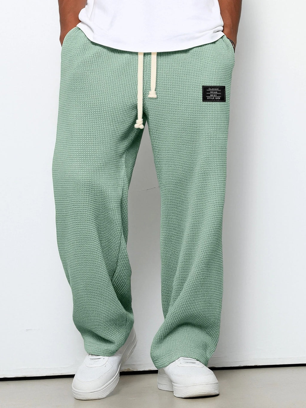 Green textured sweatpants with a brand logo worn by a person on a white background