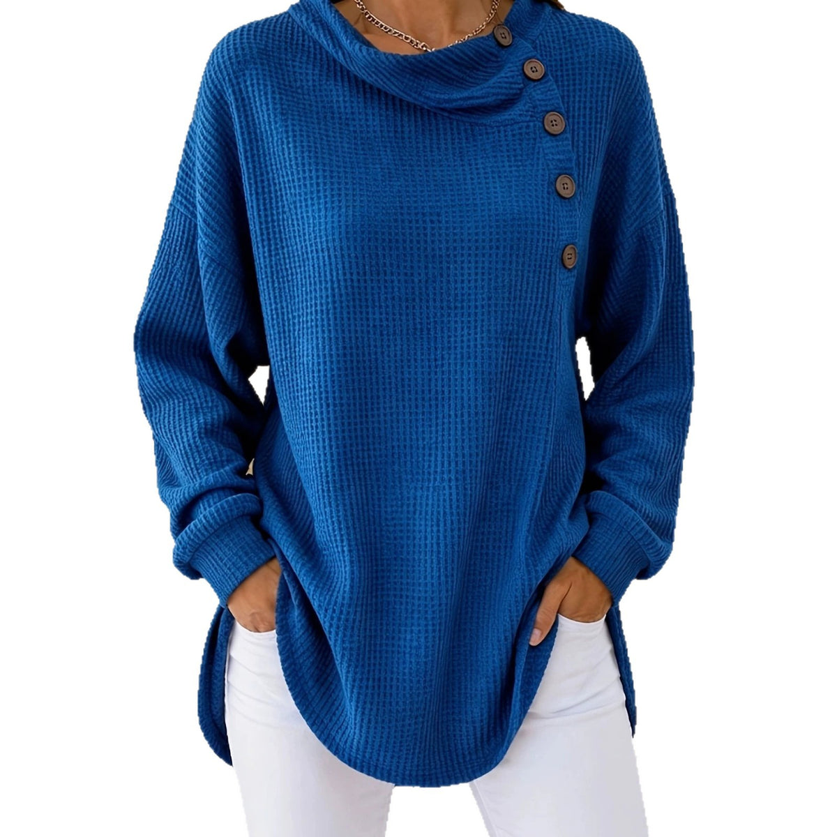 A woman wearing a blue waffle-knit cowl-neck sweater with three brown buttons down the side, paired with white pants, against a plain white background.