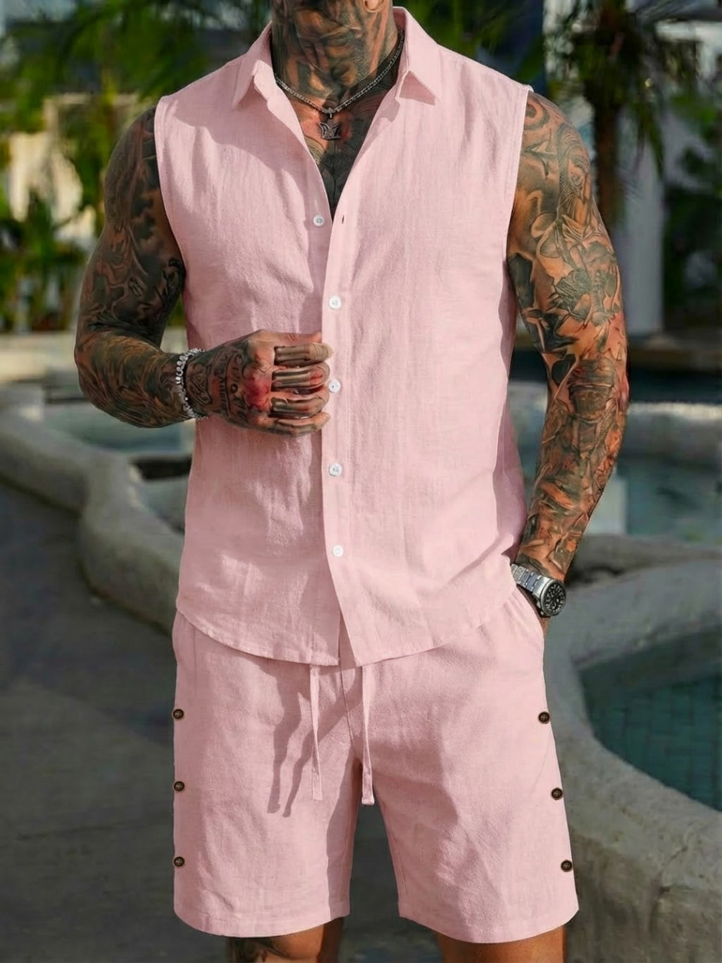 Man wearing a pink linen outfit with tattoos by a poolside.
