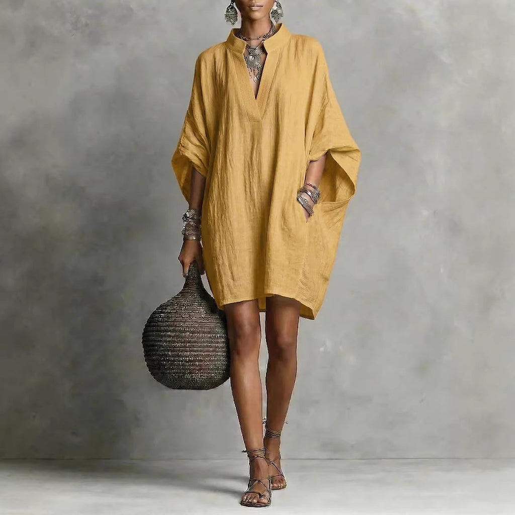 Woman wearing a mustard yellow dress holding a textured bag against a gray background