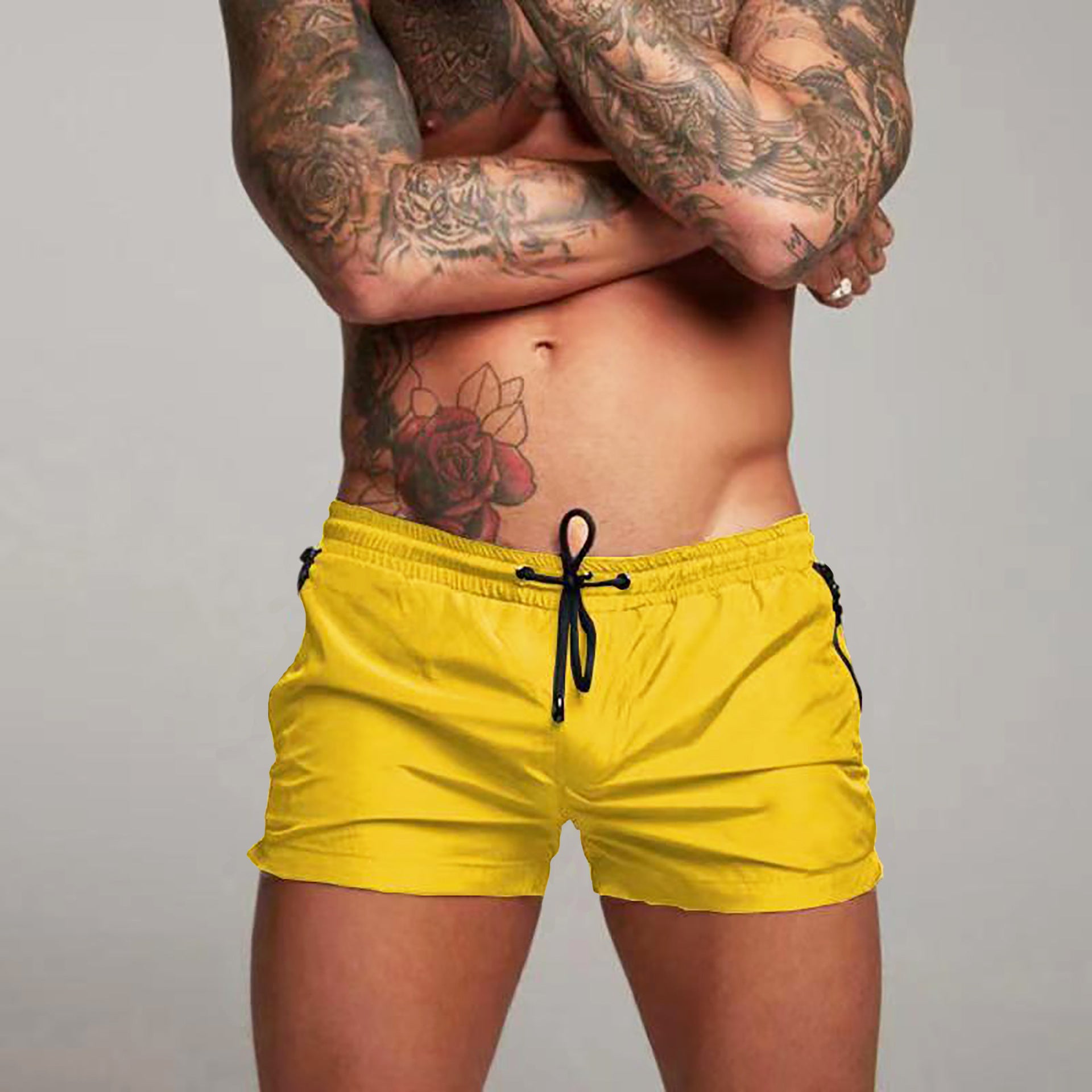 Person wearing yellow swim shorts with tattoos on a gray background
